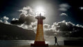 Kalk Bay harbour lighthouse silhouetted against blazing sun breaking through storm clouds with lone figure below