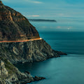 The Road Between Sea and Stone – Chapman's Peak Drive at blue hour with light trails and Kommetjie beyond