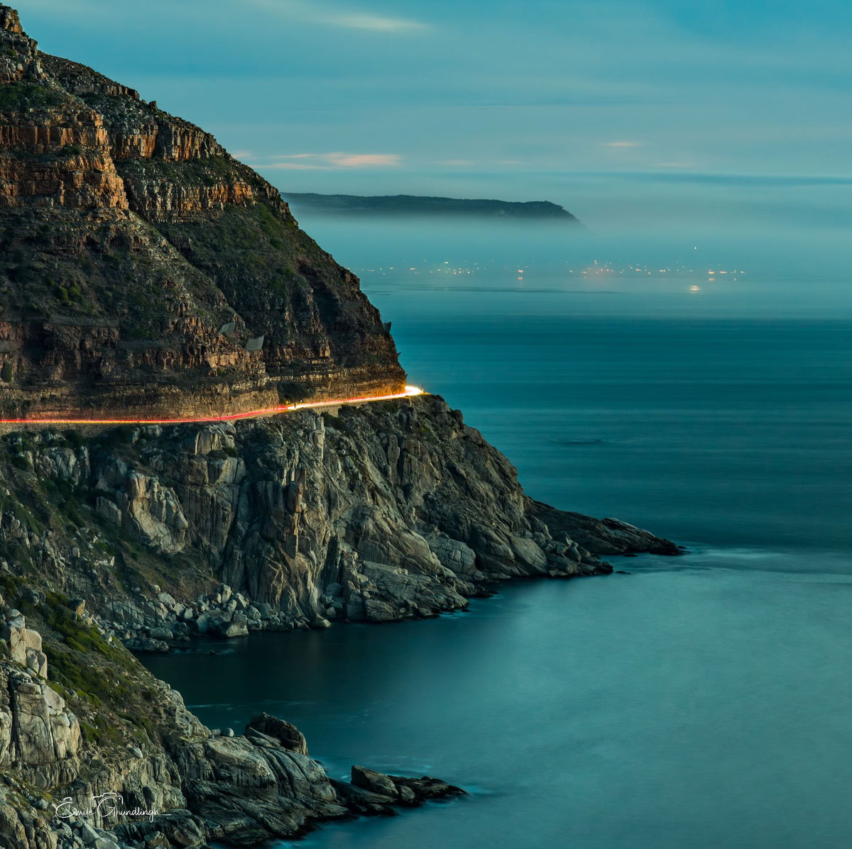 The Road Between Sea and Stone – Chapman's Peak Drive at blue hour with light trails and Kommetjie beyond