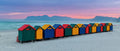 Muizenberg beach huts in a wide panoramic view at pastel dawn with pink and purple sky and Hottentots Holland Mountains silhouetted across False Bay