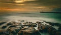 Kalk Bay harbour wall and lighthouse at golden hour with silky waves over layered rock shelves, False Bay
