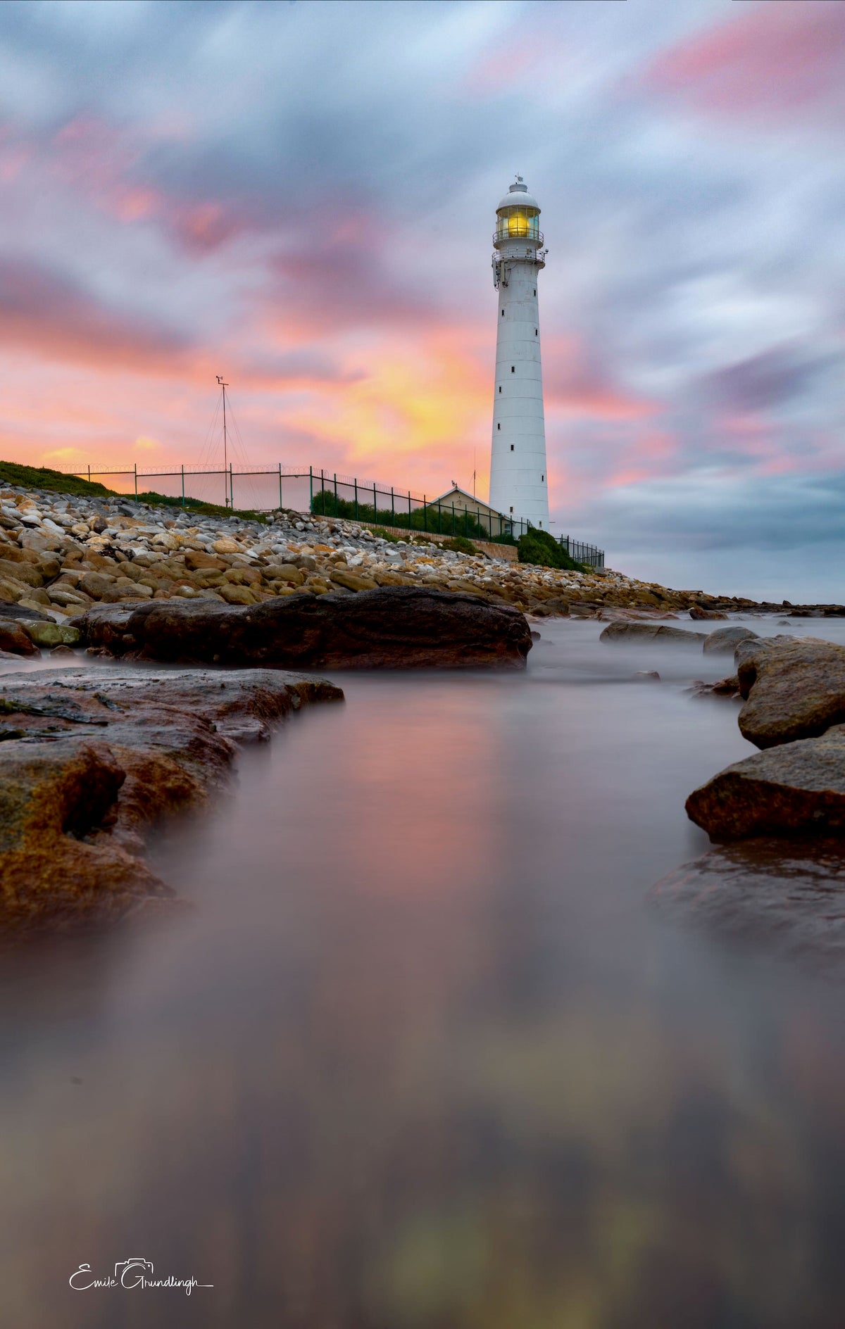 From the Rocks Slangkop – low angle view of Slangkop Lighthouse with silky water and pink sunrise sky