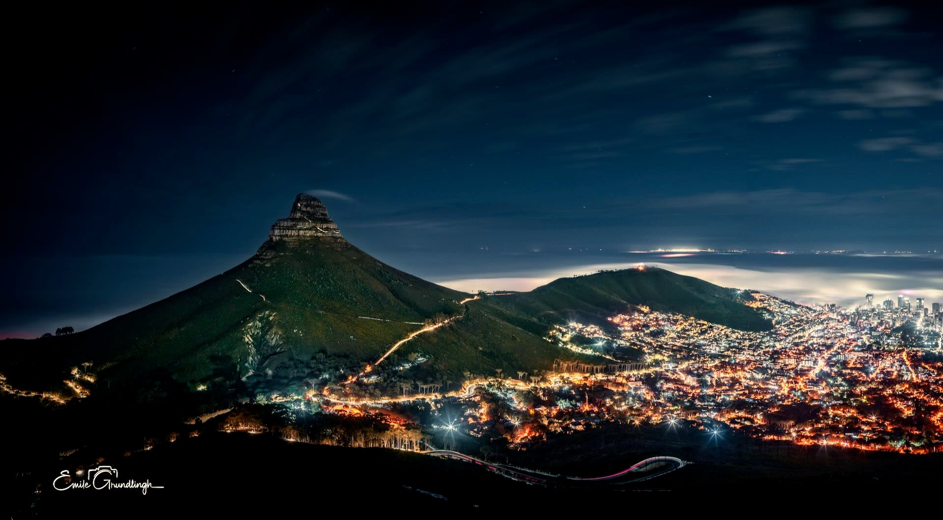 Lion's Head by night with Cape Town city lights glowing below and mist rolling in