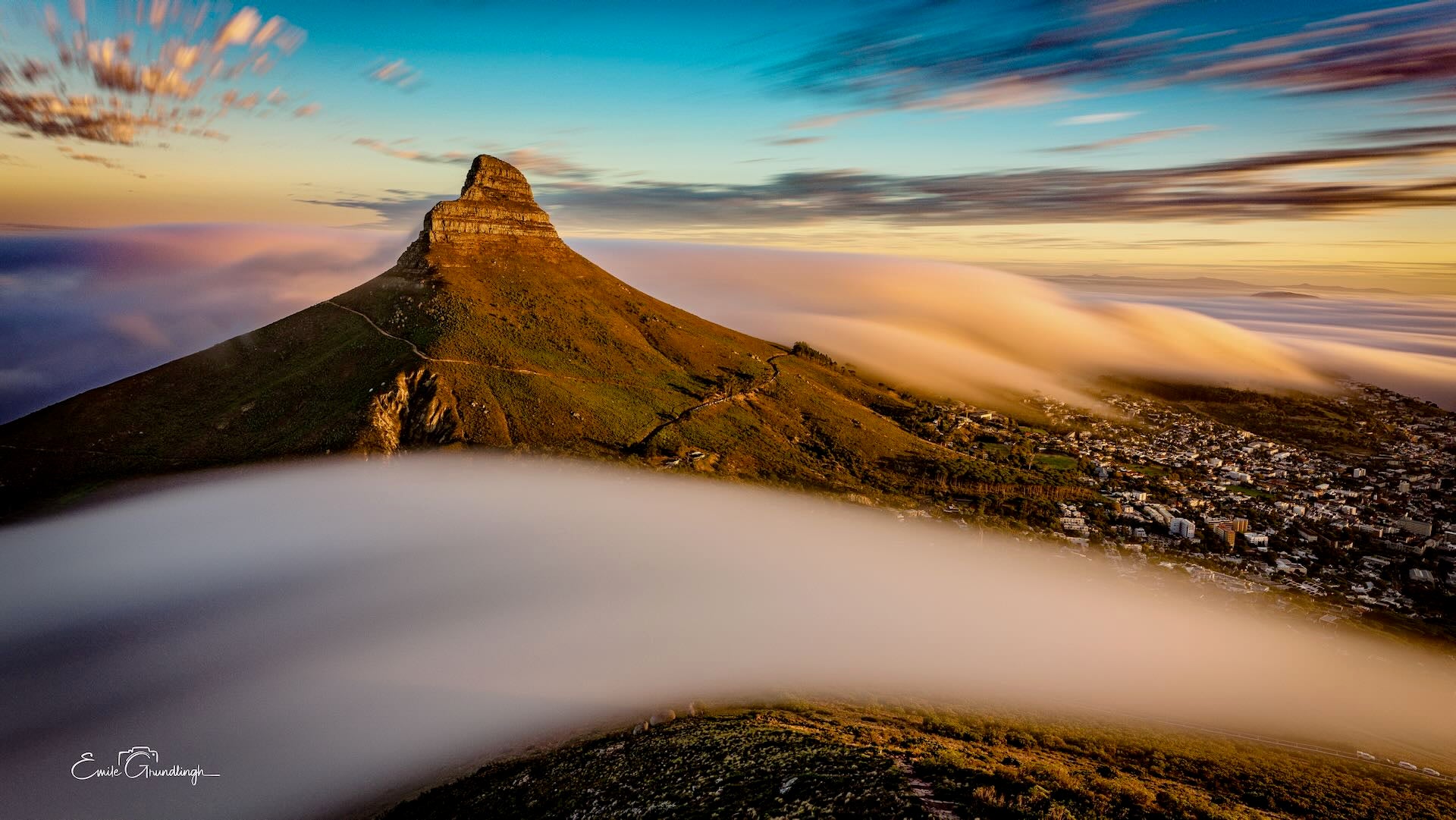 Lion's Head bathed in golden sunset light with silky mist rivers cascading around its base from Table Mountain