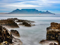 Table Mountain from rocky Bloubergstrand shores with long exposure silky water