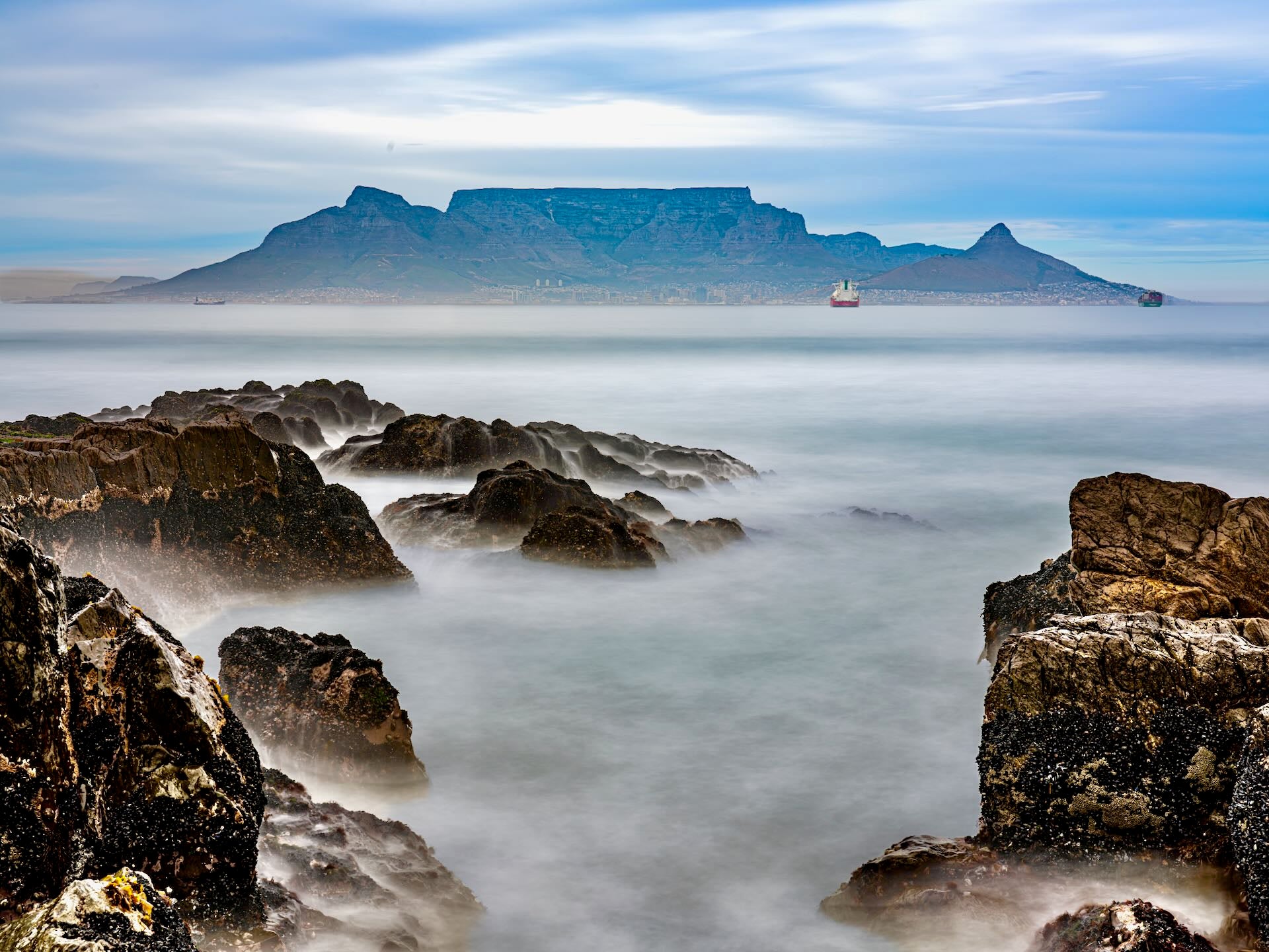 Table Mountain from rocky Bloubergstrand shores with long exposure silky water