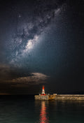 Kalk Bay harbour lighthouse glowing red under the Milky Way with reflection in still harbour water