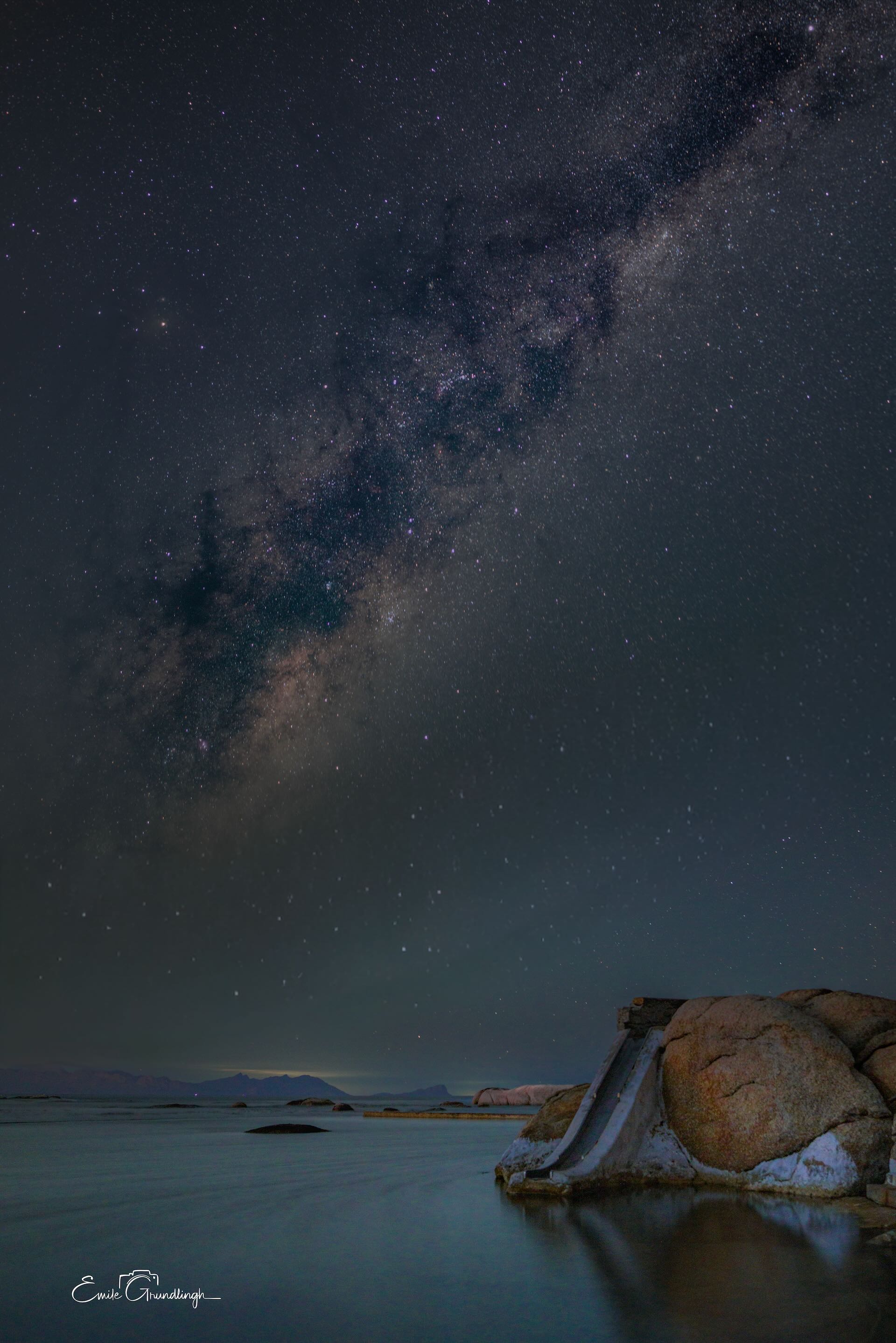 Milky Way arching over Millers Point granite boulders and calm False Bay waters at night