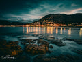 Glen Cairn coastal town lights reflecting on False Bay waters at night with rocky foreshore