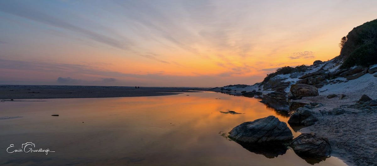 Still tidal lagoon reflecting pastel sunset on Noordhoek Beach with sand dunes and rocks by Emile Grundlingh