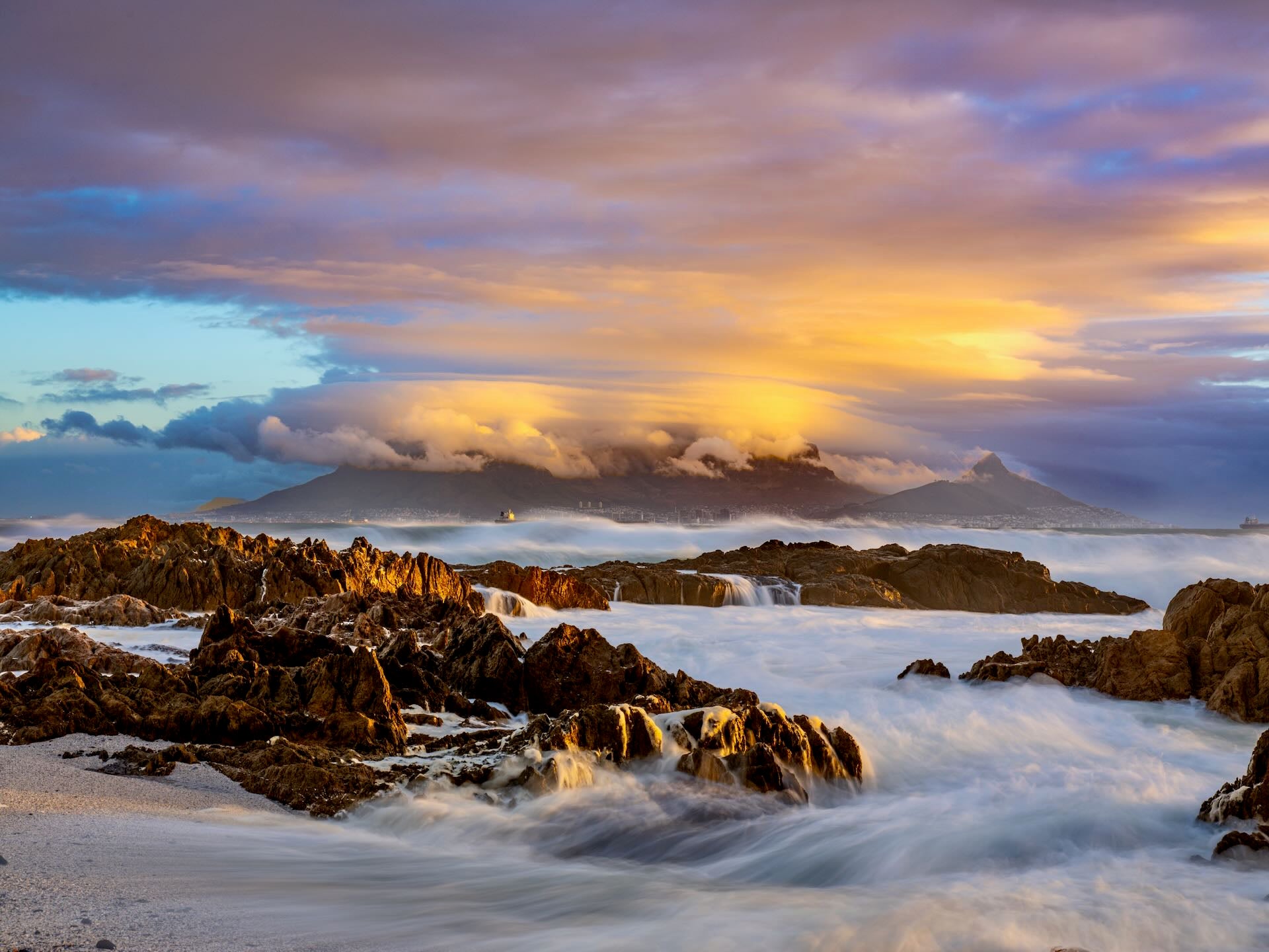 Table Mountain under golden storm clouds at sunset with wild waves at Bloubergstrand