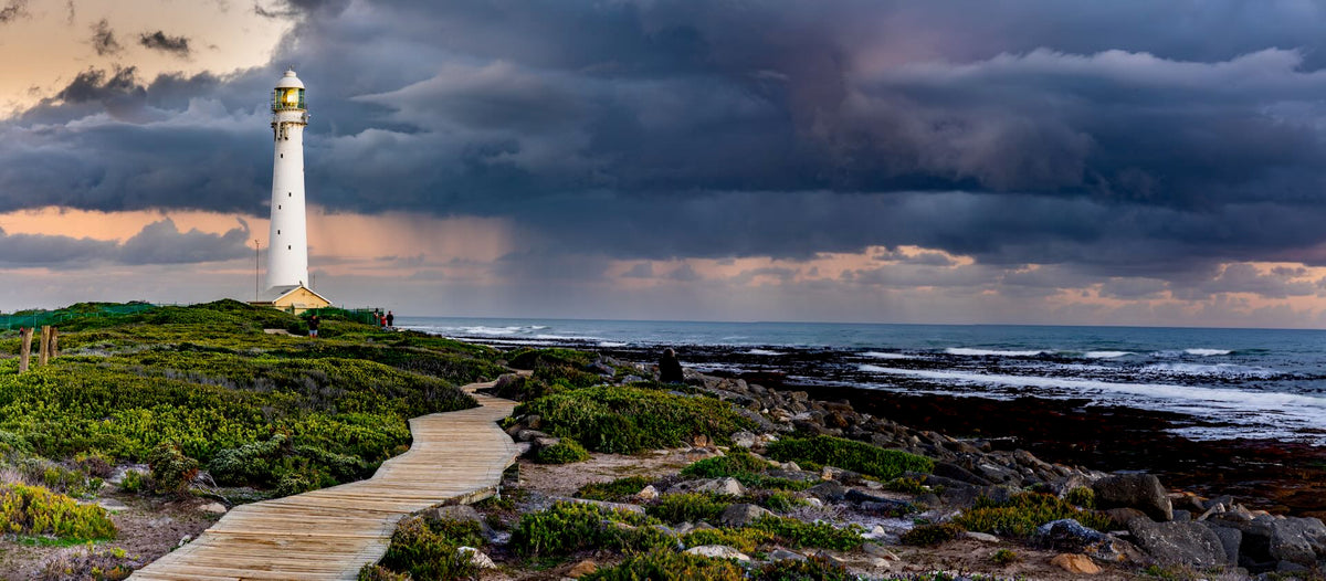 Storm Rolling In Kommetjie – dark storm clouds over Slangkop Lighthouse with boardwalk and fynbos