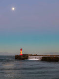 Kalk Bay harbour lighthouse under full moon in soft blue twilight sky with waves cascading over harbour wall