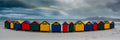 Wide panoramic view of Muizenberg beach huts on an empty beach with a perfect rainbow arching over False Bay and mountains under storm clouds
