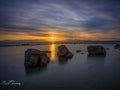 Three granite boulders in Glen Cairn tidal pool at sunset with golden reflection over False Bay