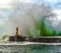 Massive emerald green wave erupting over Kalk Bay harbour wall dwarfing the lighthouse beacon, False Bay
