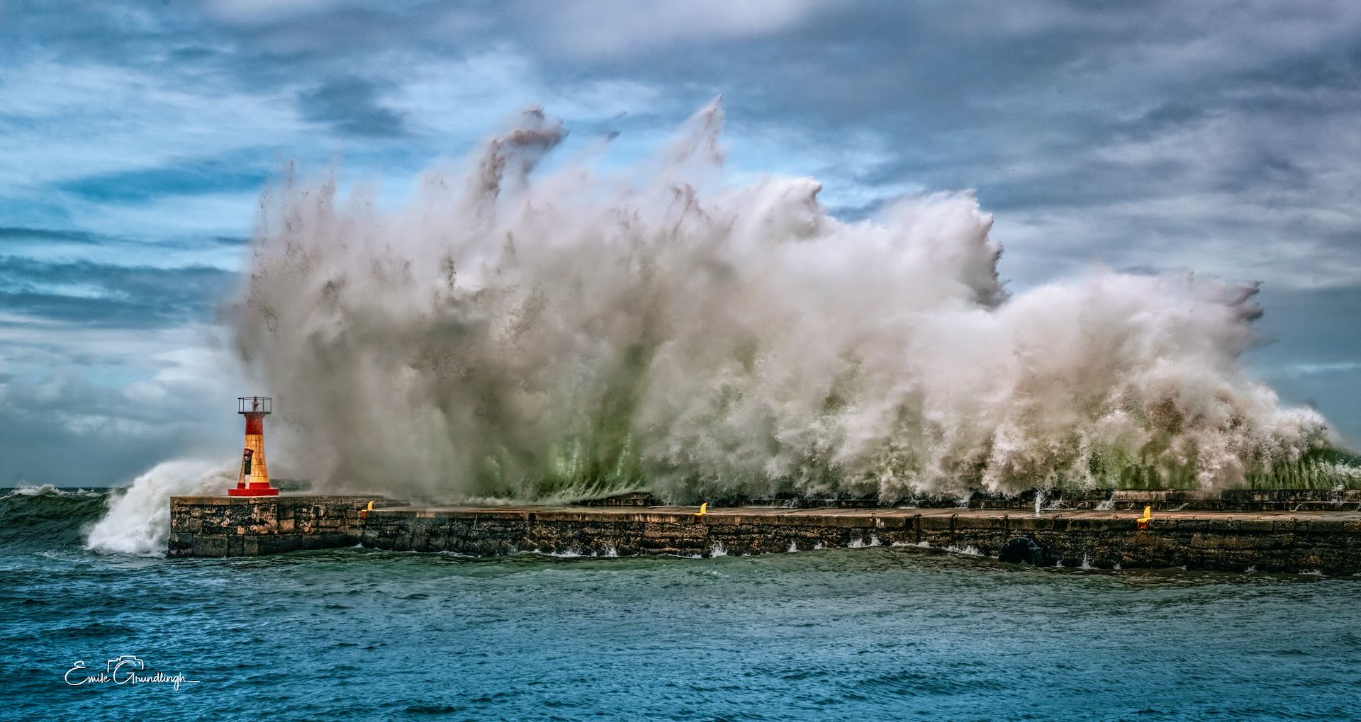 Massive wave completely engulfing Kalk Bay harbour wall with lighthouse barely visible, False Bay storm