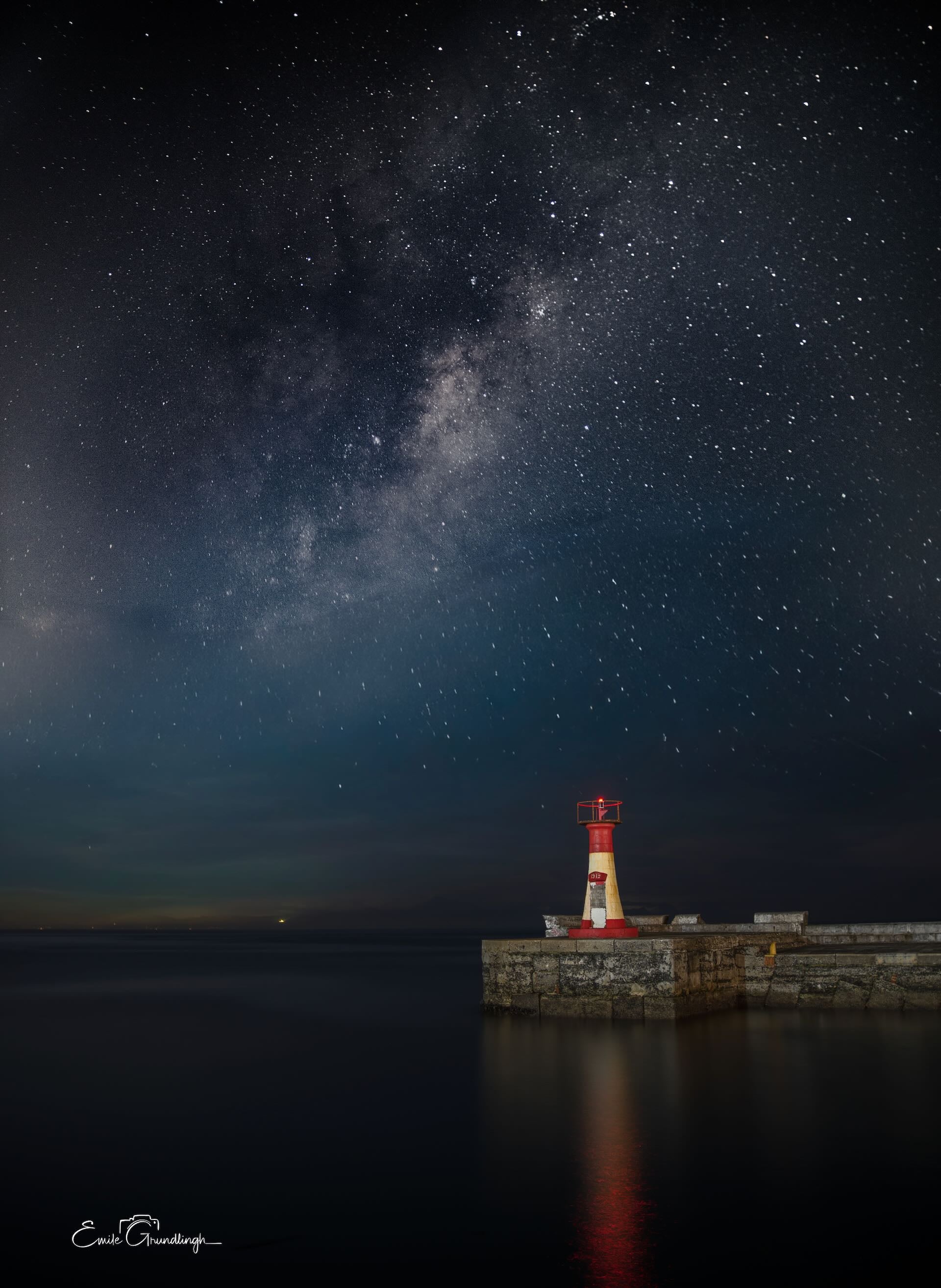 Kalk Bay harbour lighthouse standing alone on harbour wall beneath the Milky Way at night