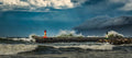 Massive waves crashing over Kalk Bay harbour wall with red and green lighthouses and dramatic rolling storm cloud