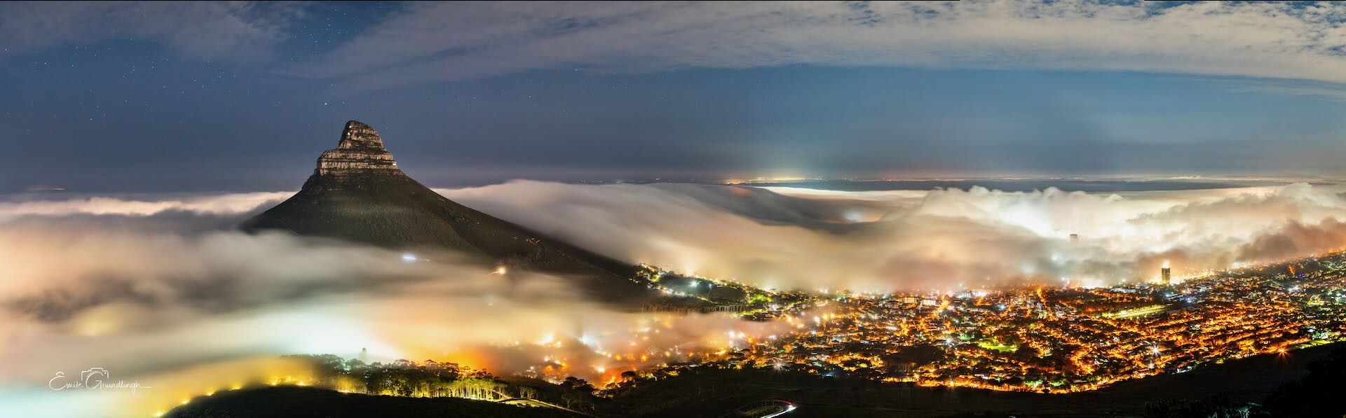 Lion's Head rising above a sea of mist over Cape Town at night wide panorama