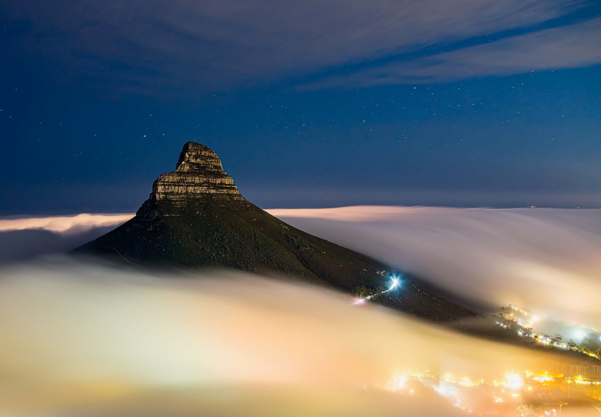 Lion's Head floating above glowing sea of mist under starry night sky Cape Town
