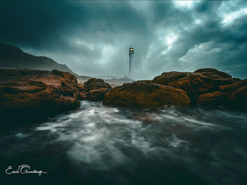 Between the Rocks Kommetjie – Slangkop Lighthouse framed by boulders under dramatic storm sky