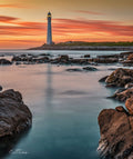 Slangkop Golden Hour – Slangkop Lighthouse framed by boulders at sunset with silky water and ghost reflection