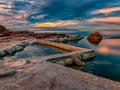 Wooleys Pool at dramatic sunrise with pink and teal clouds reflected in still water surrounded by red sandstone rocks and False Bay