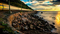 Motion-blurred train along the False Bay coastline at golden hour with rocky sea wall and silky ocean