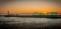 Massive emerald green wave exploding over Kalk Bay harbour wall at sunset with lighthouse in background