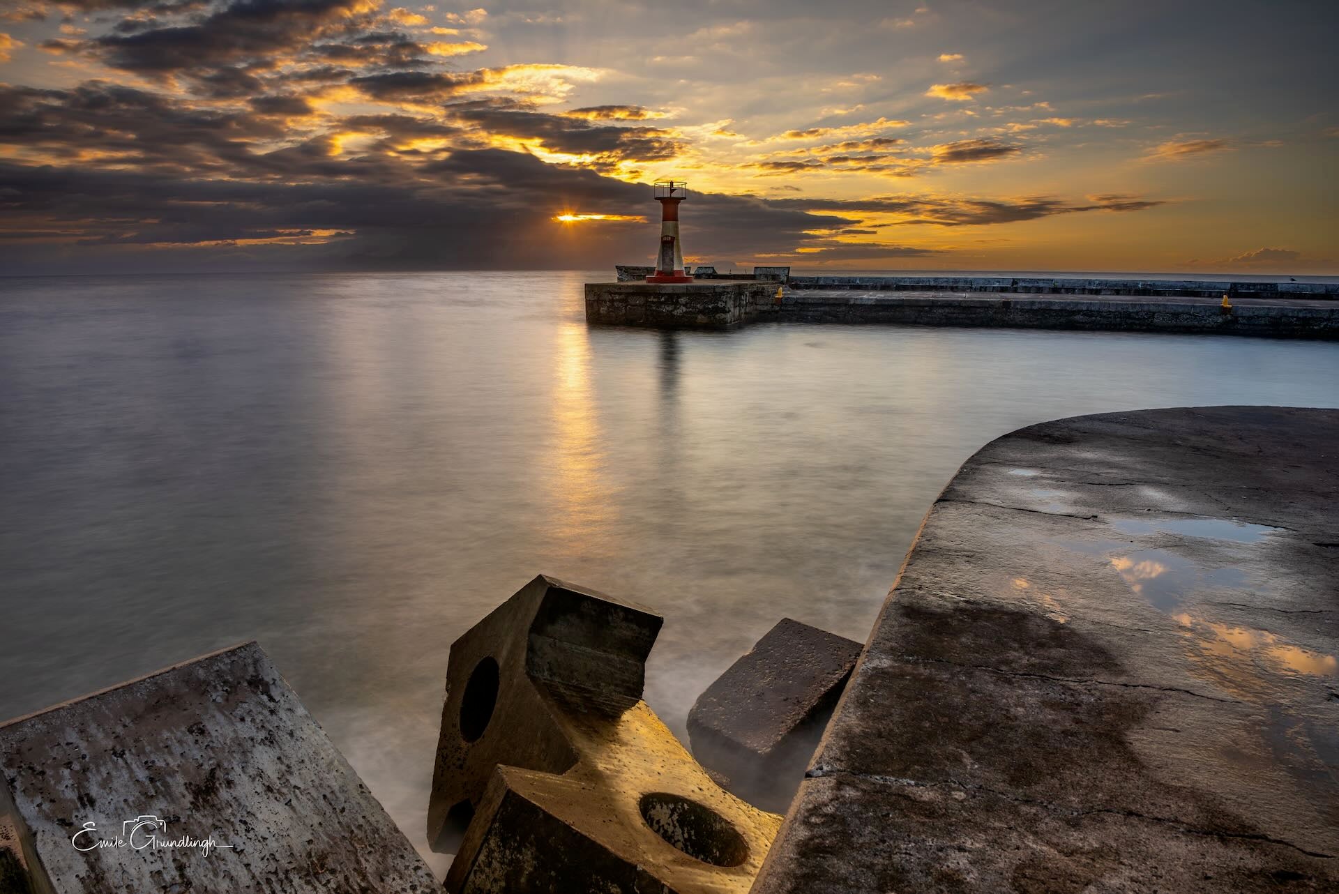 Kalk Bay harbour lighthouse at golden sunset with silky water and mooring bollards in foreground