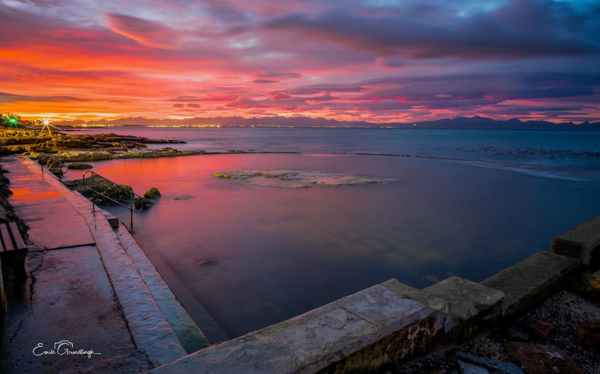 Wooleys Pool at crimson and purple sunrise over False Bay with city lights and Hottentots Holland mountains