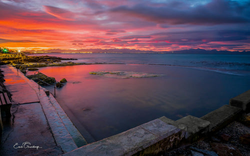 Wooleys Pool at crimson and purple sunrise over False Bay with city lights and Hottentots Holland mountains