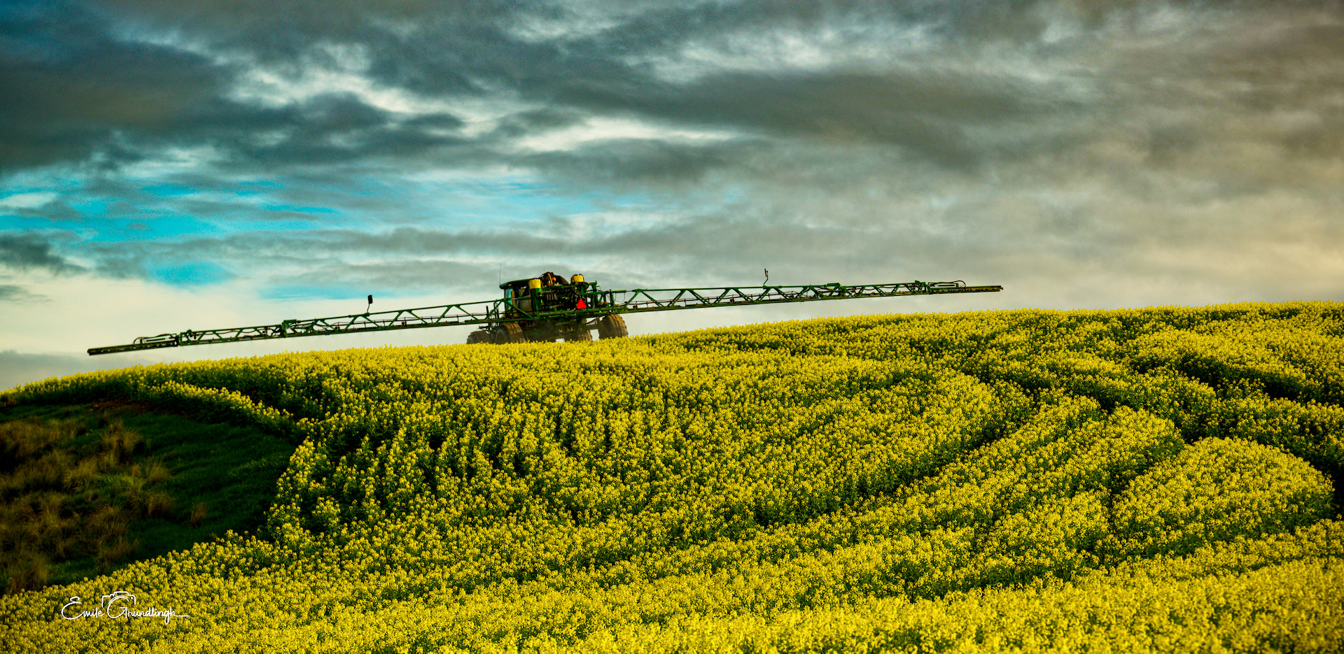 Crop sprayer silhouetted on a canola ridge under a dramatic stormy sky