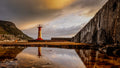 Kalk Bay lighthouse perfectly reflected in still rock pool on harbour wall with dark wall and mountain village backdrop