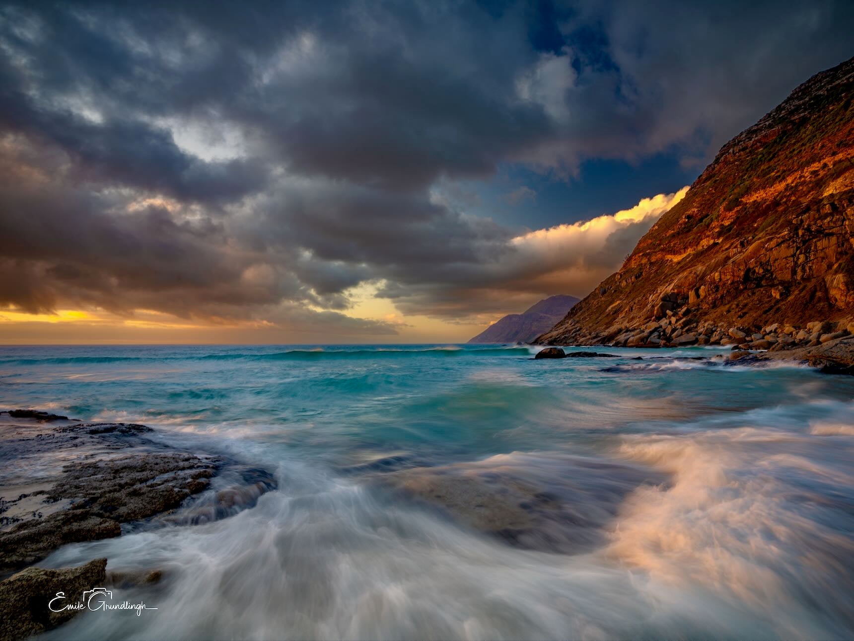 Golden sunlit cliffs above turquoise stormy waves on the Cape Peninsula coastline at sunset