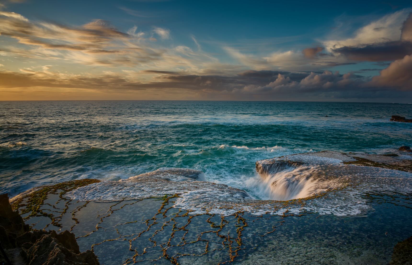 Ocean waves pouring into a natural rock cauldron at Arniston coastline at golden sunset