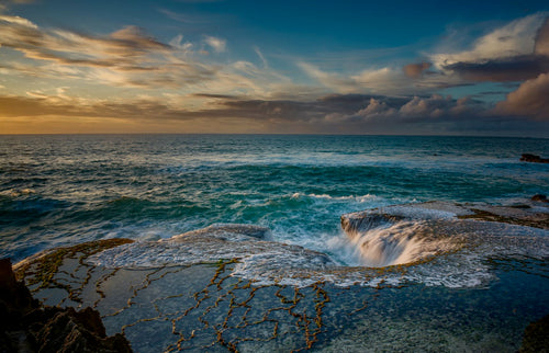 Ocean waves pouring into a natural rock cauldron at Arniston coastline at golden sunset