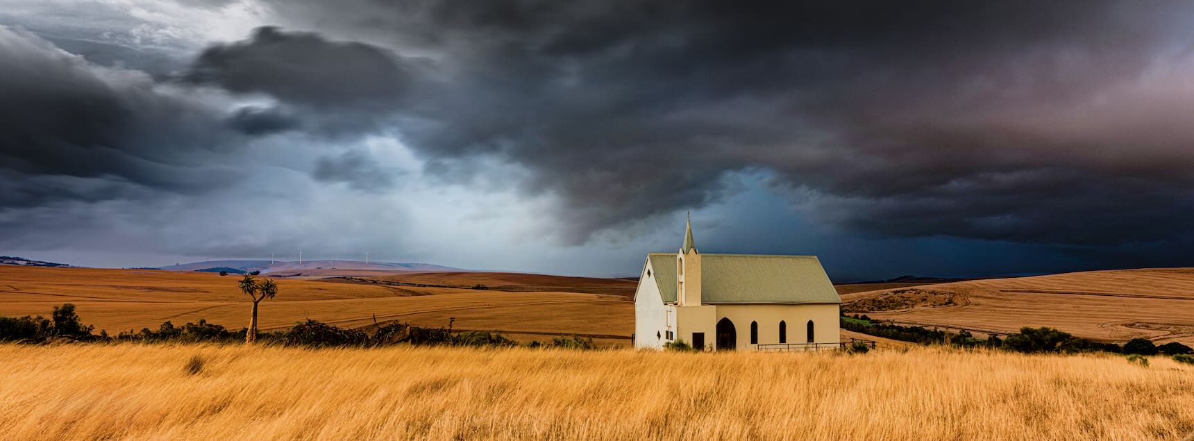 White chapel on golden plains under dramatic storm clouds