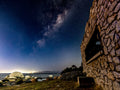 Milky Way arching over ancient stone ruins at Millers Point with granite boulders on False Bay shoreline at night