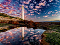 Slangkop Lighthouse at Kommetjie perfectly reflected in a rock pool under a dramatic pink and blue sunset sky