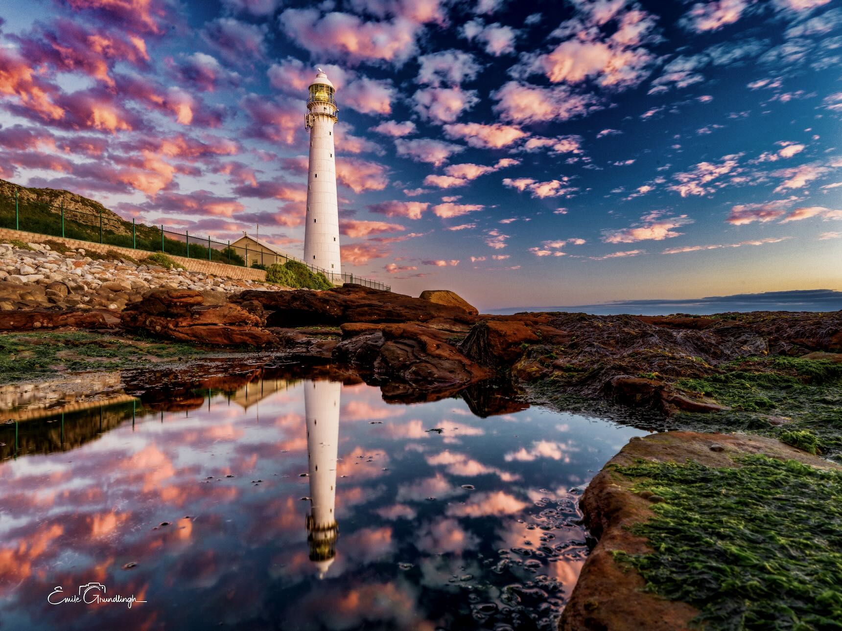 Slangkop Lighthouse at Kommetjie perfectly reflected in a rock pool under a dramatic pink and blue sunset sky