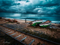Two abandoned green fishing boats on boat launch rails at Makriels Beach with rain sweeping across False Bay under storm sky
