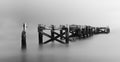 Crumbling wooden jetty fading into silky white mist in a long exposure black and white photograph