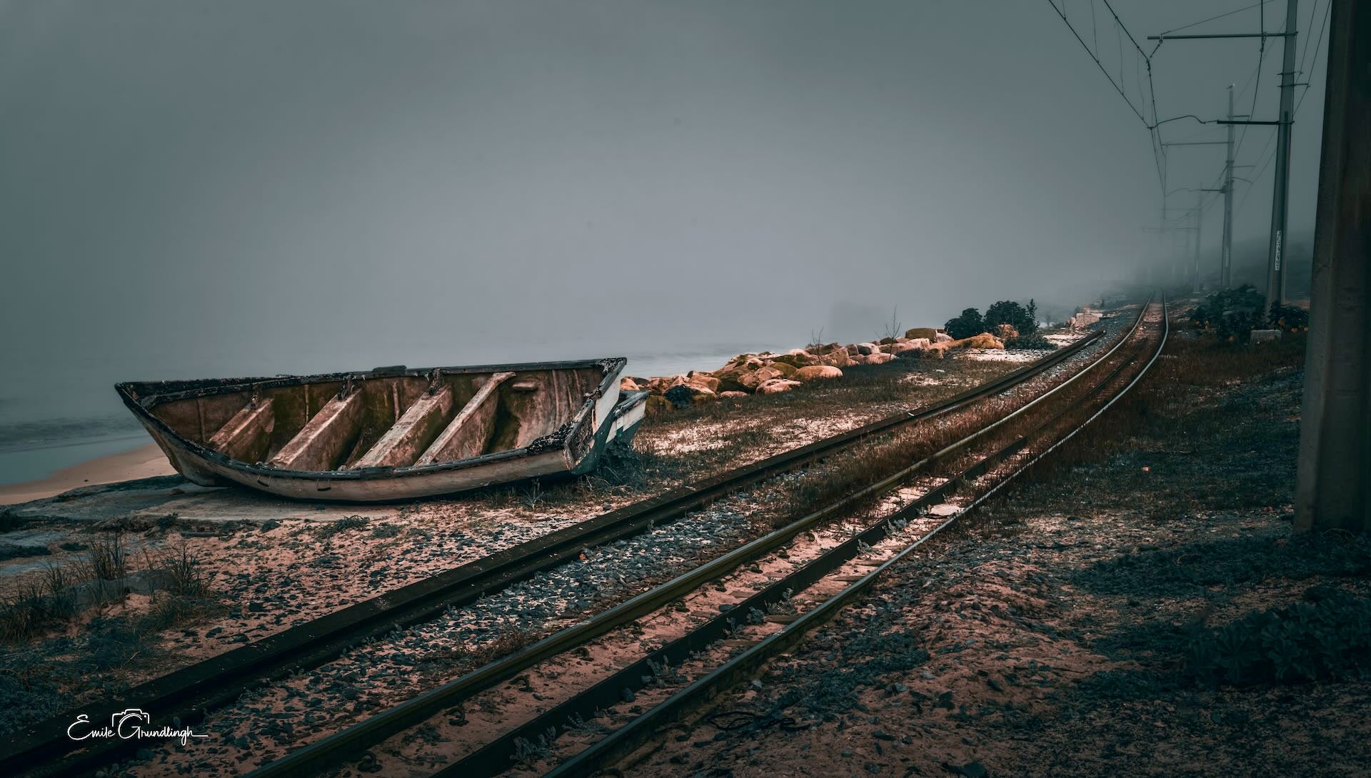 Wrecked wooden boat beside coastal railway tracks disappearing into thick sea mist at Makriels Beach, False Bay