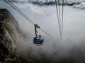 Table Mountain cable car suspended between rocky cliff and swirling clouds