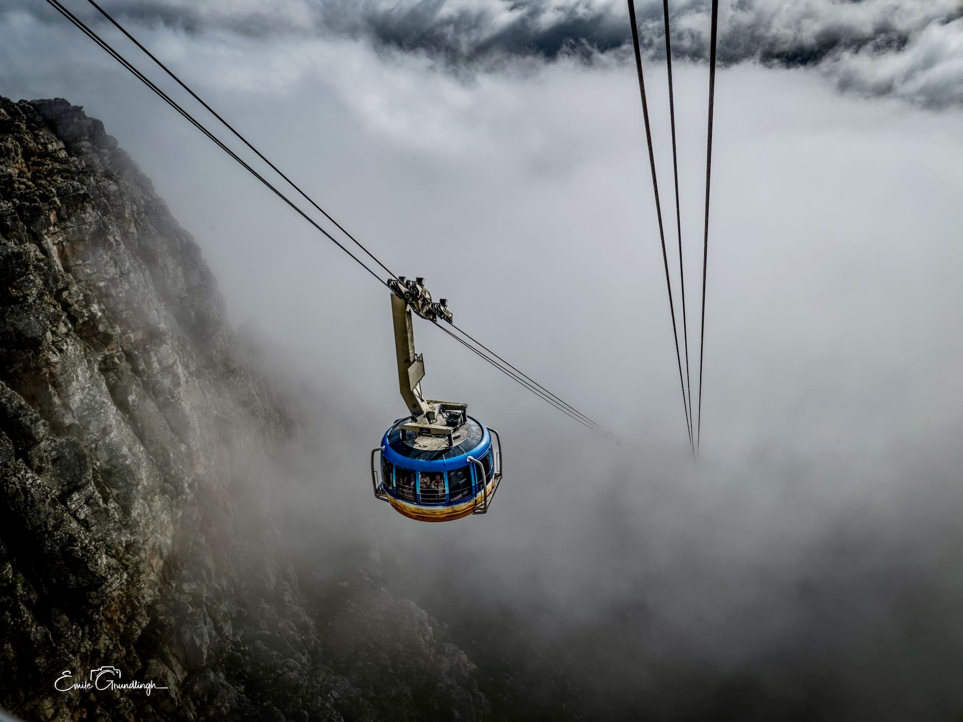 Table Mountain cable car suspended between rocky cliff and swirling clouds