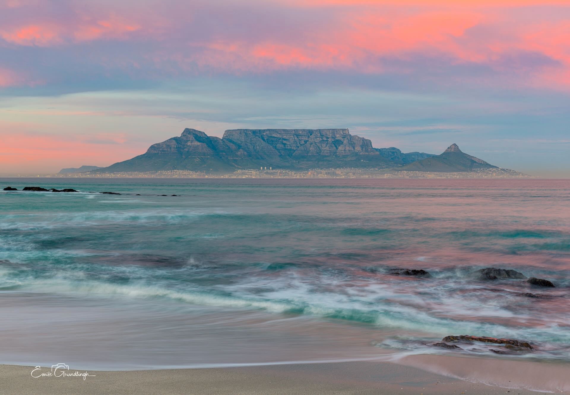 Table Mountain and Lion's Head at soft pink sunrise from Blouberg Beach with silky waves