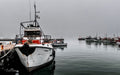 Weathered fishing trawler moored in misty fog-shrouded Kalk Bay harbour with ghostly fleet fading into grey mist