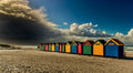 Row of colourful Muizenberg beach huts on empty sand with dramatic storm clouds rolling in from the left